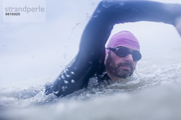 Erwachsener Mann  der im Meer schwimmt  Neoprenanzug und Brille trägt.