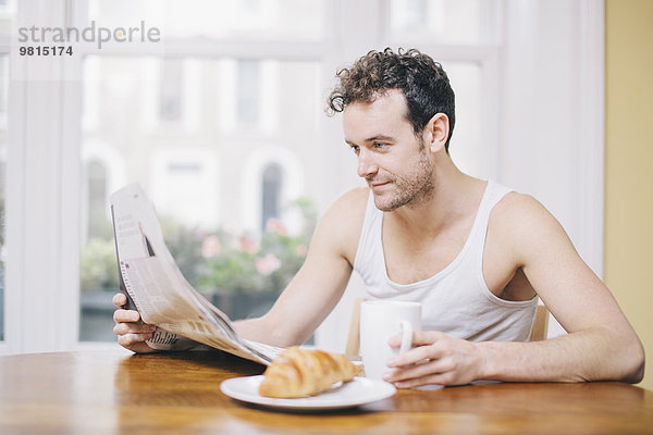 Junger Mann liest Zeitung beim Frühstück