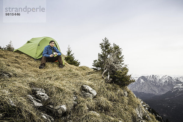 Junger Wanderer beim Kaffeetrinken vor dem Zelt auf der Klammspitze  Oberammergau  Bayern  Deutschland