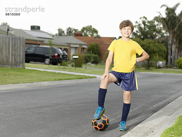 Portrait des Jungen mit Fuß auf Fußball auf Vorstadtstraße