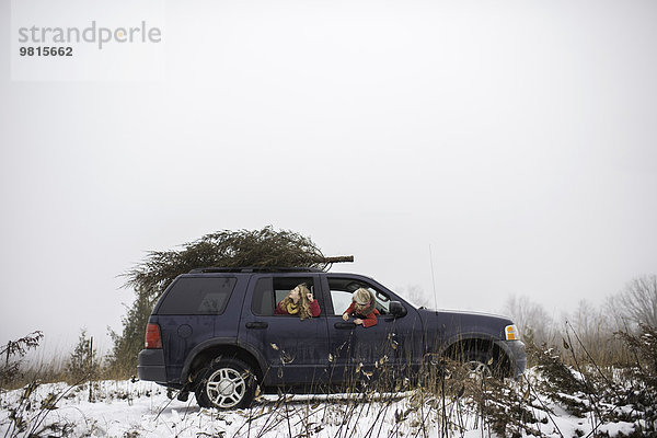 Zwei Mädchen im Auto mit Weihnachtsbaum auf dem Dach