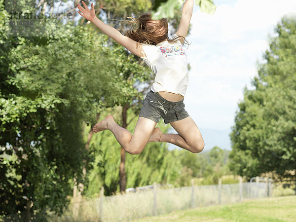 Teenager-Mädchen springt mit ausgestreckten Armen  in der Luft  im Freien