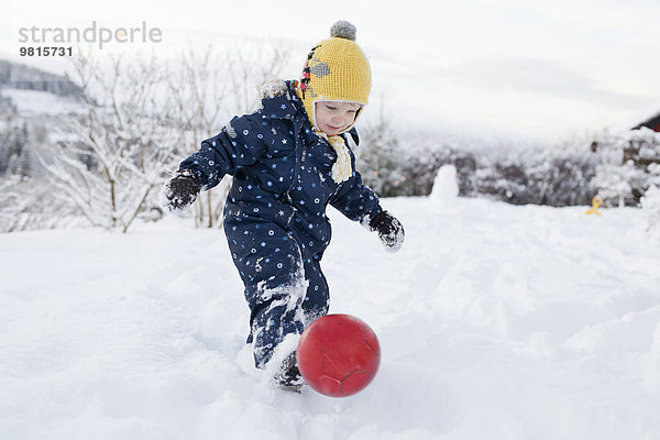Junge tritt seinen Ball in den Schnee