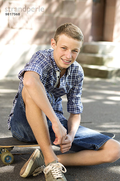 Lächelnder Teenager auf dem Skateboard sitzend
