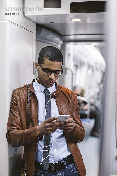 Geschäftsmann mit Smartphone und Kopfhörer  der Musik in der U-Bahn hört.