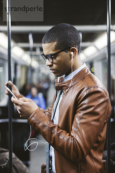 Portrait eines Geschäftsmannes mit Smartphone und Kopfhörer  der Musik in der U-Bahn hört.
