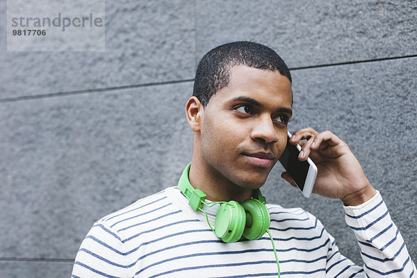 Portrait eines jungen Mannes mit grünen Kopfhörern beim Telefonieren mit Smartphone