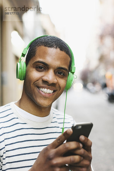 Porträt eines lächelnden jungen Mannes  der Musik mit grünen Kopfhörern auf der Straße hört.