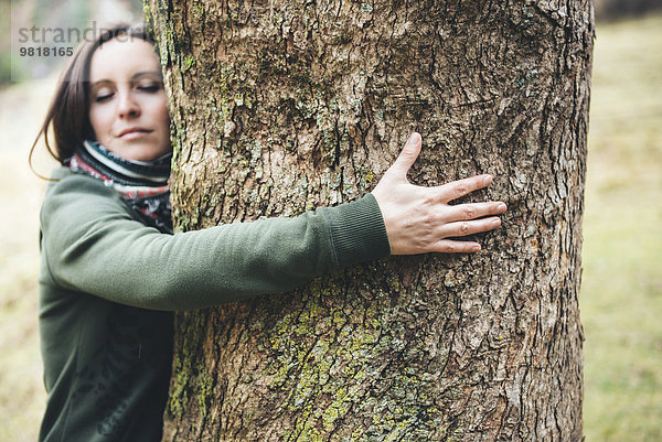 Frau umarmt einen großen Baumstamm