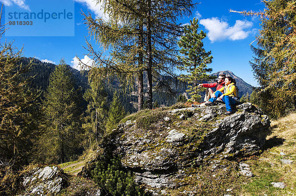 Österreich  Altenmarkt-Zauchensee  junges Paar auf einem Felsen sitzend mit Blick auf die Landschaft