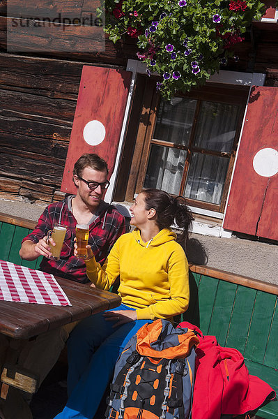Österreich  Altenmarkt-Zauchensee  junges Paar mit Biergläsern vor der Berghütte