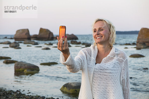 Estland  Kaesmu  blonde Frau mit einem Selfie mit Smartphone am Strand