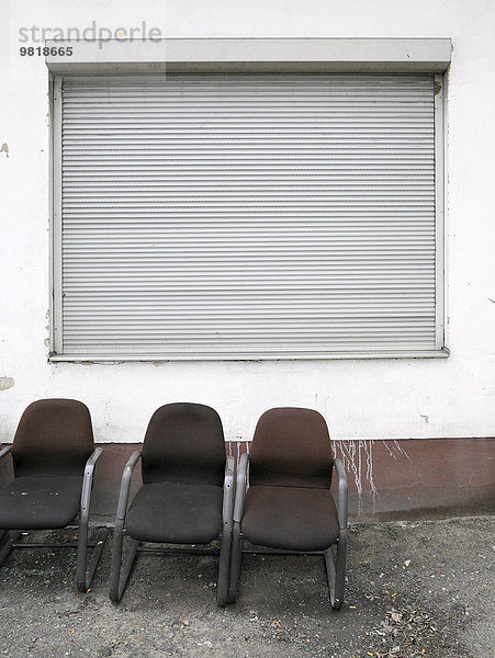 Deutschland  drei alte Stühle vor der Fassade mit geschlossenem Rollladen