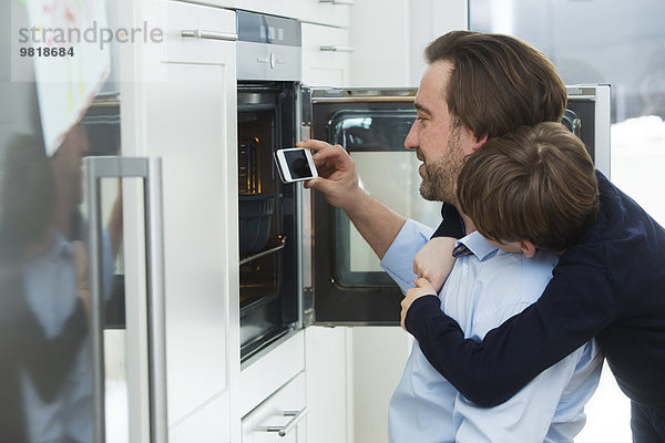 Vater und Sohn fotografieren Kuchen im Ofen mit Smartphone