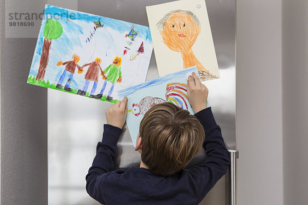 Der Junge hat seine Zeichnungen am Kühlschrank repariert.