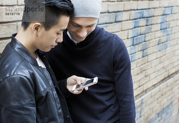China  Hongkong  junges männliches schwules Paar  das auf der Straße steht und auf das Smartphone schaut.