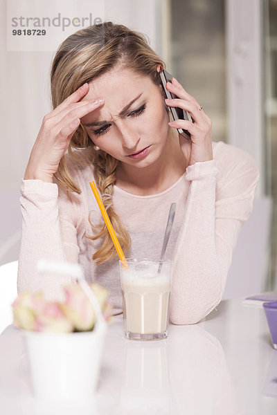 Unglückliche blonde Frau sitzt in einem Café und telefoniert mit dem Smartphone.