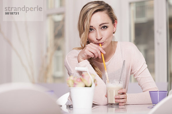 Porträt einer blonden Frau  die in einem Café sitzt und Latte Macchiato trinkt.