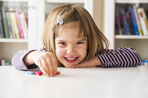 Lächelndes kleines Mädchen spielt mit Schokoladenknöpfen