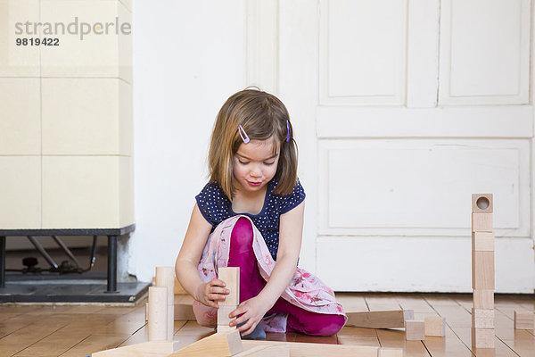 Kleines Mädchen hockt auf dem Boden und spielt mit Holzbausteinen.