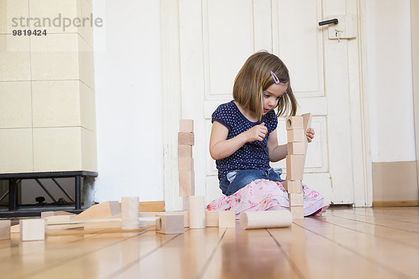 Kleines Mädchen hockt auf dem Boden und spielt mit Holzbausteinen.