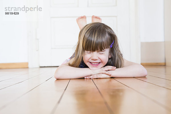 Lächelndes Mädchen auf Holzboden liegend  die Augen schließend