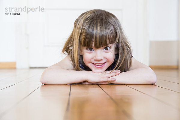 Lächelndes Mädchen auf Holzboden liegend