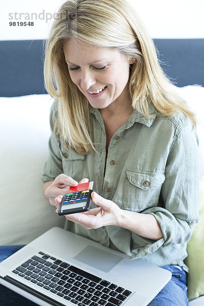 Lächelnde blonde Frau mit Laptop über Online-Banking