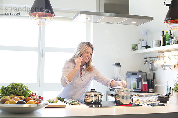 Lächelnde Frau am Handy beim Kochen in der Küche