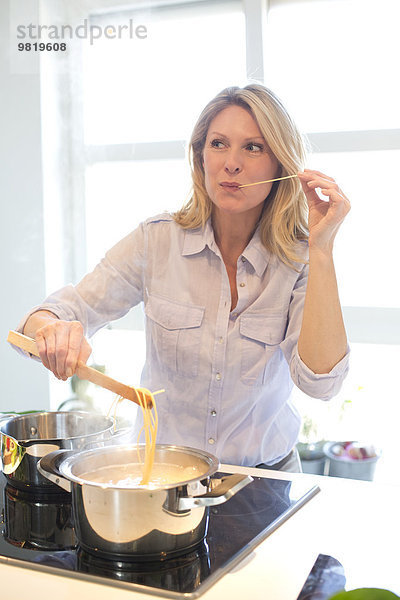 Frau kocht in der Küche und schmeckt Spaghetti