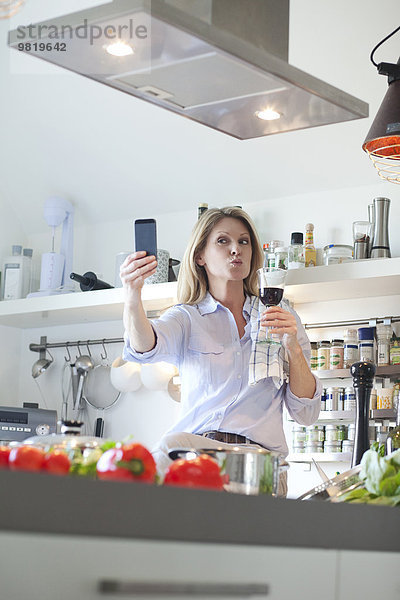 Frau in der Küche mit einem Glas Rotwein bei einem Selfie