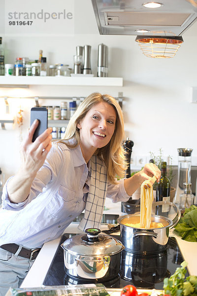 Lächelnde Frau in der Küche Kochen Spaghetti mit einem Selfie