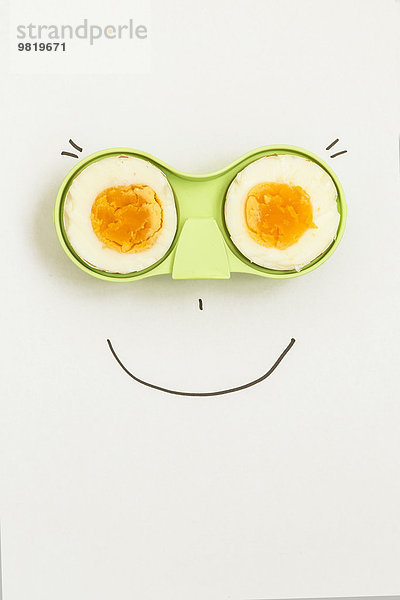 Zwei Hälften eines Eies in grünem Halter mit fröhlichem Gesicht drumherum