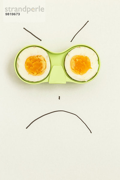 Zwei Hälften eines Eies in grünem Halter mit einem wütenden Gesicht drum herum