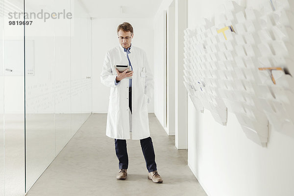 Reifer Mann im Laborkittel stehend im Flur mit Blick auf das digitale Tablett