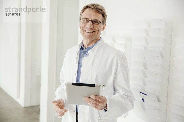 Lächelnder reifer Mann im Laborkittel mit digitalem Tablett