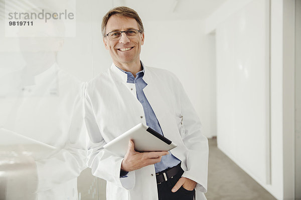 Lächelnder reifer Mann im Laborkittel mit digitalem Tablett