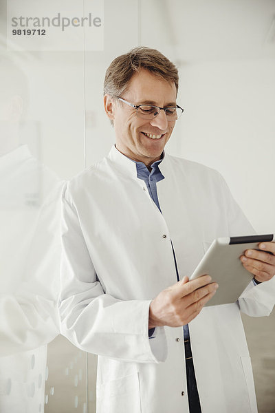 Lächelnder reifer Mann im Laborkittel mit Blick auf digitales Tablett