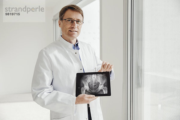 Reifer Mann im Laborkittel mit Röntgenbild auf seinem digitalen Tablett