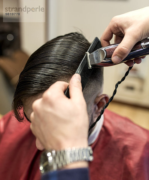 Friseur beim Rasieren der Haare eines jungen Mannes in einem Friseursalon