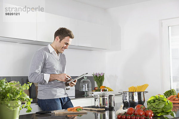 Lächelnder Mann mit digitalem Tablett in der Küche
