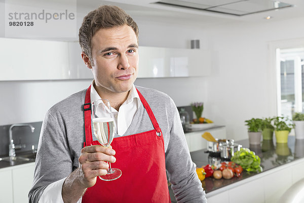 Porträt eines Mannes  der ein Glas Sekt in der Küche anbietet.