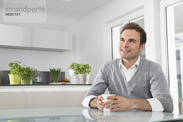 Lächelnder Mann in der Küche mit einer Tasse Kaffee