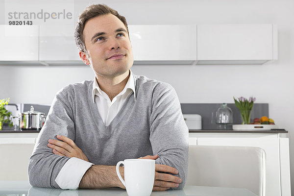 Porträt eines lächelnden Mannes in der Küche mit einer Tasse Kaffee