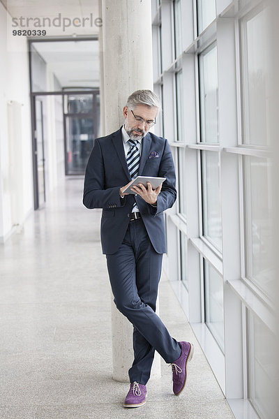 Geschäftsmann  der sich mit Hilfe eines digitalen Tabletts gegen die Säule lehnt
