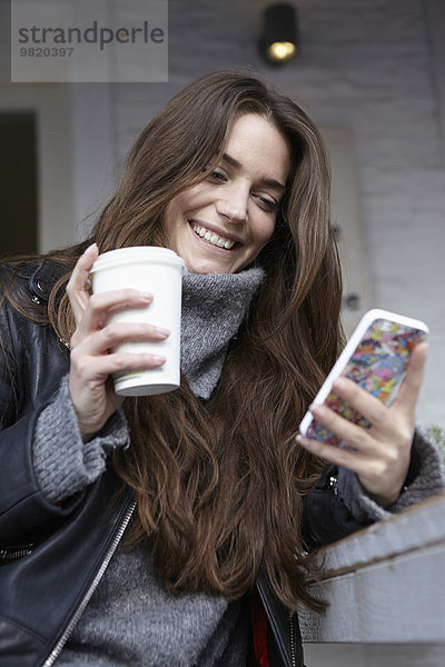 Deutschland  Düsseldorf  Junge Frau mit Kaffeetasse über Smartphone