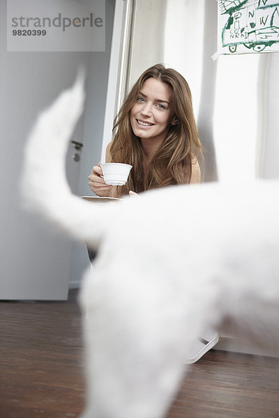 Junge Frau in der Küche trinkt Tasse Kaffee  Hund im Vordergrund