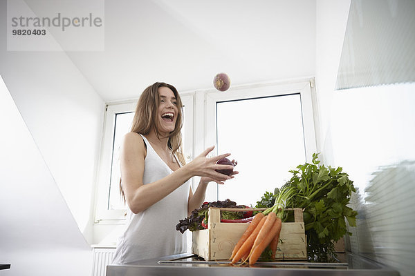 Fröhliche junge Frau in der Küche mit Kiste voller frischem Gemüse
