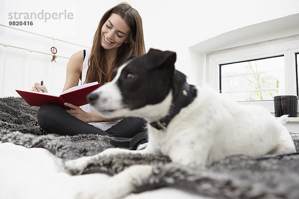 Junge Frau auf dem Bett sitzend mit Hundeschreibtagebuch
