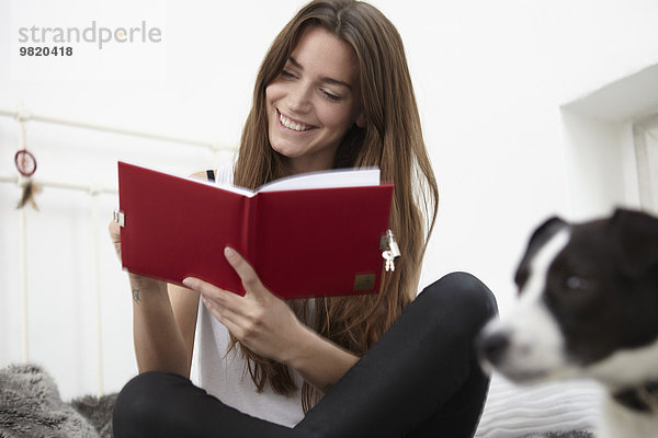 Junge Frau auf dem Bett sitzend mit Hundeschreibtagebuch